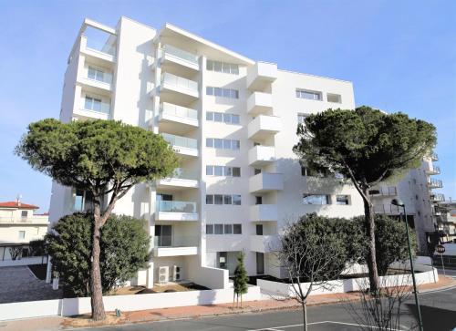 un immeuble d'appartements blanc avec des arbres devant lui dans l'établissement Zero5.Zero5, à Lignano Sabbiadoro