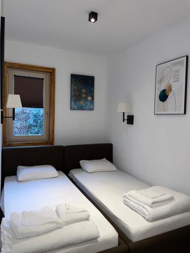 two beds in a room with white sheets and a window at The Nest Apartman, Župa Wellness & Spa Kopaonik in Kopaonik