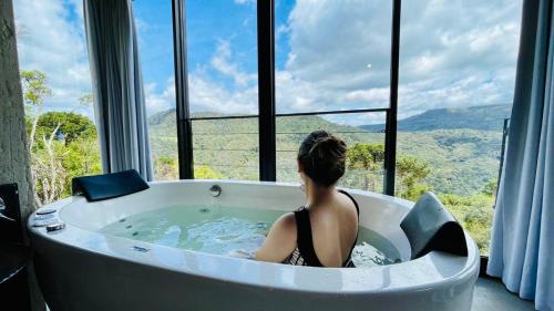 a woman sitting in a bath tub in front of a window at Cabana Efatah - Pousada Colina dos Ventos in Urubici