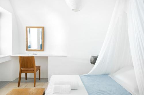 a bedroom with a bed with a mirror and a chair at Gabbiano Traditional Cave Houses in Oia