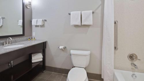 a bathroom with a toilet and a sink and a mirror at Best Western PLUS Austin Airport Inn & Suites in Austin