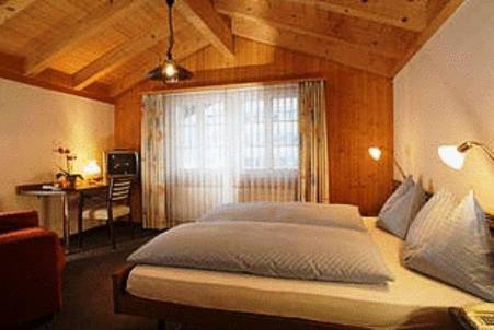 a bedroom with a bed with a window and a desk at Hotel Steinbock Grindelwald in Grindelwald