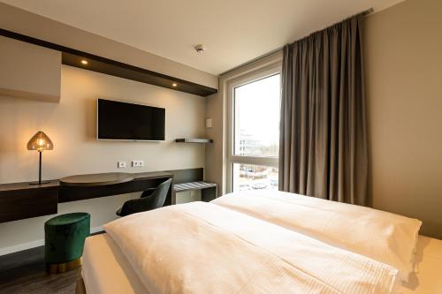 a hotel room with a bed and a desk and a television at MASEVEN München Messe Trudering in Munich
