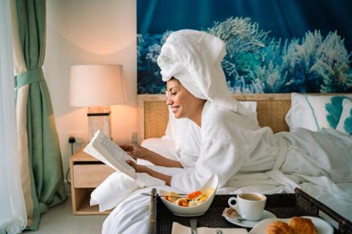 a woman sitting in bed reading a book at AQUA Boutique Hotel in Glacis