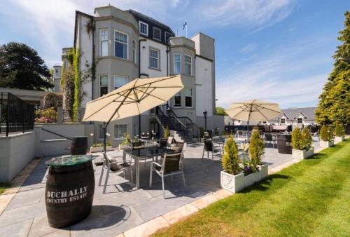 a patio with tables and chairs and an umbrella at Ryder Cup Lodge Duchally - Free access to Leisure Club Swimming Pool Hot Tub Steam Room - Starlink Satellite Internet - Sky Glass Now DOG FRIENDLY for 2025 in Auchterarder