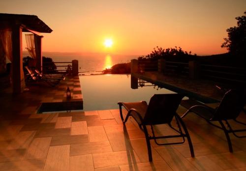 a sunset over a pool with chairs and a table at Red Rose Artistsvillas in Gaios