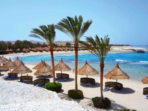 einen Strand mit Sonnenschirmen, Palmen und dem Meer in der Unterkunft Movenpick Resort El Quseir in Al-Qusair