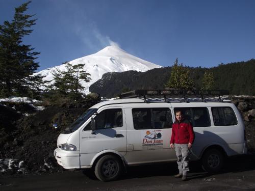 a man standing next to a van with a snow covered mountain at Hostal & Cabañas Don Juan in Villarrica