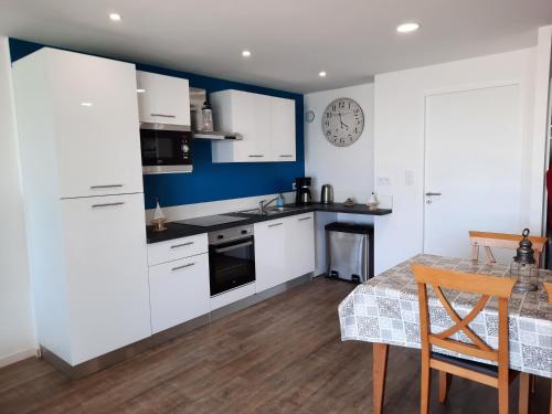 une cuisine avec des placards blancs, une table et une horloge dans l'établissement Magnifique appartement face à la mer !! Résidence Charmette, à Saint-Hilaire-de-Riez