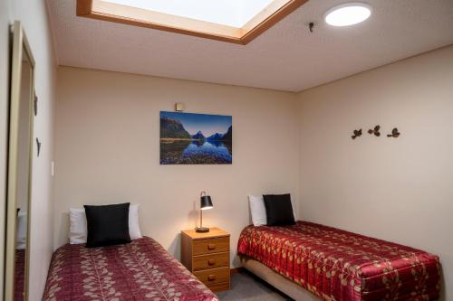 a bedroom with two beds and a night stand with a lamp at ASURE Aspiring Court Motel in Haast