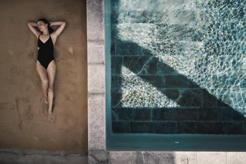 a woman laying on the sand next to a swimming pool at Nomad Mykonos - Small Luxury Hotels of the World in Kalo Livadi