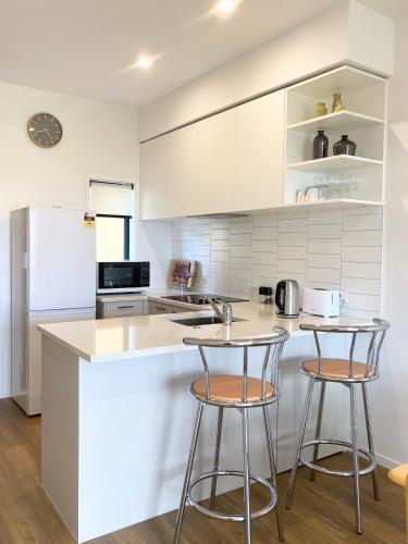 a kitchen with two bar stools and a refrigerator at Stunning Townhouse - Walking to Botany Shopping Center in Auckland