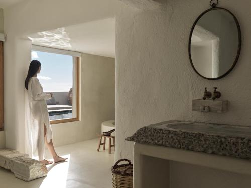 a woman standing in a room looking out a window at Nomad Mykonos - Small Luxury Hotels of the World in Kalo Livadi