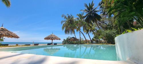 a swimming pool next to a beach with palm trees at Jungle Paradise Beach Resort & Spa at Mbweni Ruins Hotel Zanzibar in Zanzibar City