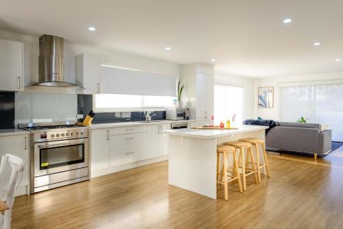 a kitchen with white cabinets and a kitchen island with bar stools at Georges Bay Apartments in St Helens