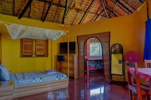 1 dormitorio con paredes amarillas, 1 cama y espejo en Colibri Lodge, en Ambatoloaka