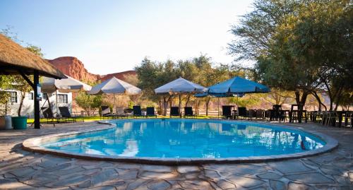 einen Pool mit Sonnenschirmen, Tischen und Stühlen in der Unterkunft Namib Desert Camping2Go in Solitaire