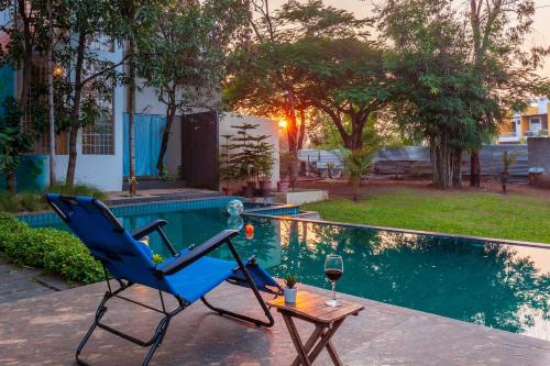 a blue chair and a glass of wine next to a pool at Morning Dew Retreat by StayVista - Modern interiors, Indoor games, Lush greenery, Pool & Gazebo await your escape in Nashik