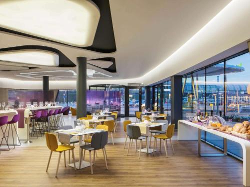 un restaurante con mesas, sillas y ventanas en ibis Styles Budapest Airport, en Vecsés