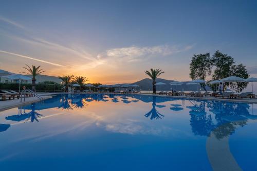 a pool at a resort with a sunset in the background at Pilot Beach Resort in Georgioupolis