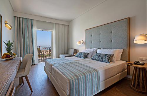 a hotel room with a large bed and a balcony at Pilot Beach Resort in Georgioupolis