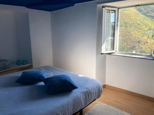 a bedroom with a bed with blue pillows and a window at Casa da Carvalha - Ádela in Açor