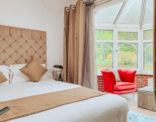 a bedroom with a bed and a red chair and a window at Trivelles Waterhall Country Gatwick Hotel & airport parking in Crawley