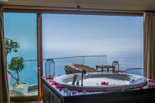 a bath tub in a room with a view of the ocean at Lissiya Hotel in Faralya