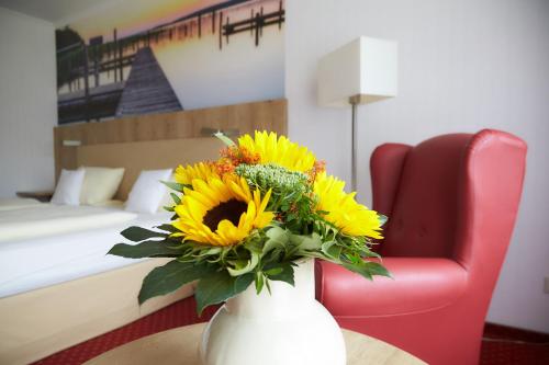 a vase filled with yellow flowers on a table with a red chair at Flairhotel Hubertus in Bad Zwischenahn