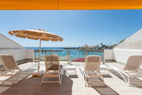 a deck with chairs and an umbrella and the ocean at BLUE SEA I in Puerto de Mogán