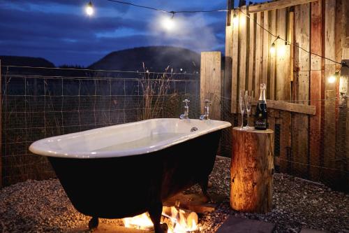 Unique tiny house with wood fired roll top bath in heart of the Cairngorms في بالاتر: حوض استحمام مع النار بجانب السياج