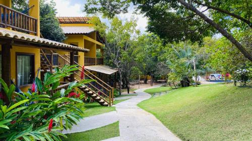 a walkway next to a yellow house with a yard at Loft Reserva Sapiranga Praia do Forte Vila Hen 102 in Mata de Sao Joao