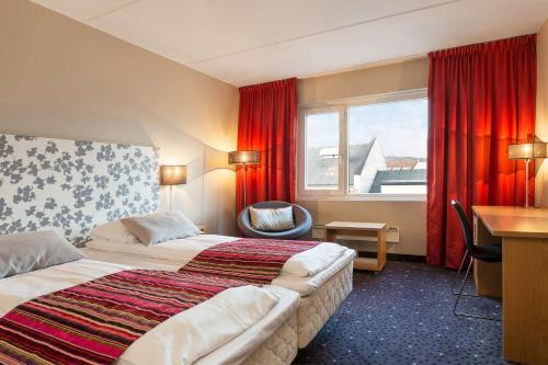 a hotel room with two beds and a desk and a window at Scandic Kirkenes in Kirkenes