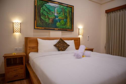 a bedroom with a white bed with a painting on the wall at Anik Homestay in Canggu