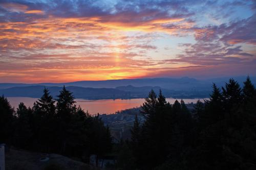 a sunset over a body of water with trees at Honeymoon Suite in West Kelowna