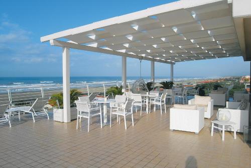 a patio with white chairs and tables and the ocean at Hotel Joseph in Marina di Pietrasanta