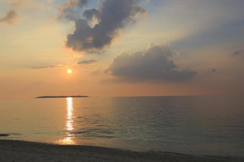a sunset on the beach with the sun setting over the ocean at パークサイドモリ in Motobu