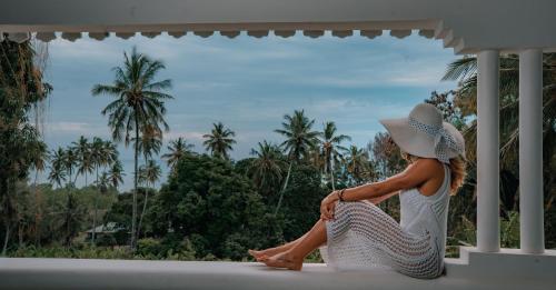 a woman sitting on a porch looking out at palm trees at The Manor House by Sansi in Zanzibar City