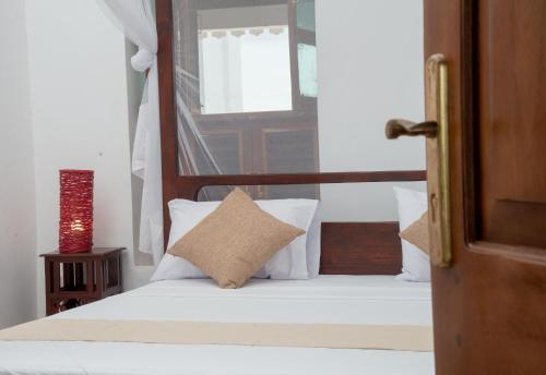 a bedroom with a bed with white pillows and a window at The Manor House by Sansi in Zanzibar City