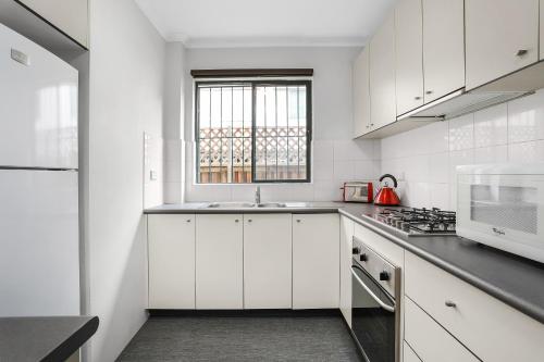 cocina blanca con armarios blancos y ventana en Spacious & Charming Alexandria 2 Bdrm Apartment - Secured Parking Space, en Sídney