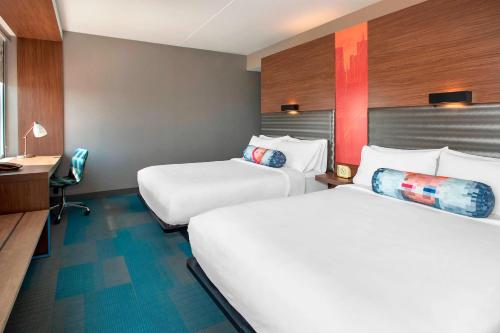 a hotel room with two beds and a desk at Aloft Buffalo Airport in Cheektowaga