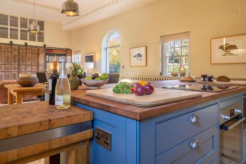 una cocina con armarios azules y una mesa con verduras en una tabla de cortar en Stunning luxury cottage in historic country estate - Belchamp Hall Stables, en Belchamp Otten