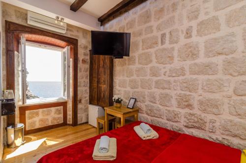 a bedroom with a stone wall and a red bed at Eddie's Sea View Rooms Old Town in Dubrovnik