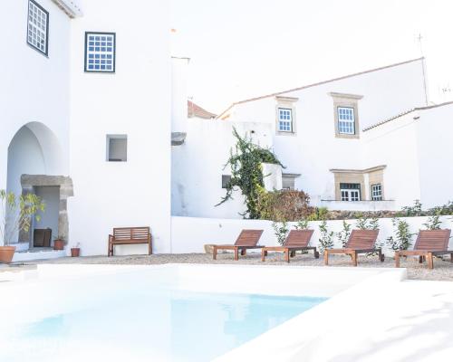 una piscina di fronte a un edificio bianco con panchine di A BURGUESA - GUESTHOUSE a Castelo de Vide