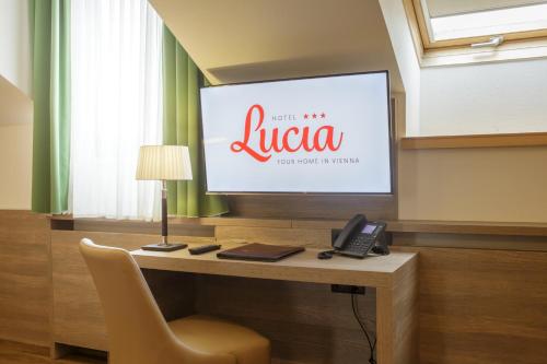 a television with a desk with a chair and a phone at Hotel Lucia in Vienna