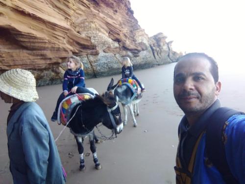 un hombre de pie junto a dos burros en la playa en dar boujdaa, en Sidi Kaouki