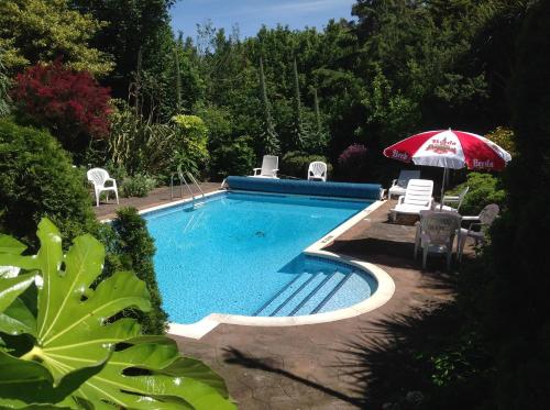 einen Pool mit einem roten Regenschirm, Stühlen und einem Sonnenschirm in der Unterkunft Hotel La Michele in St Martin Guernsey