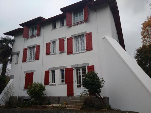 un edificio blanco con persianas rojas. en Location Chambre Sare Larhun Zola 2022 en Sare