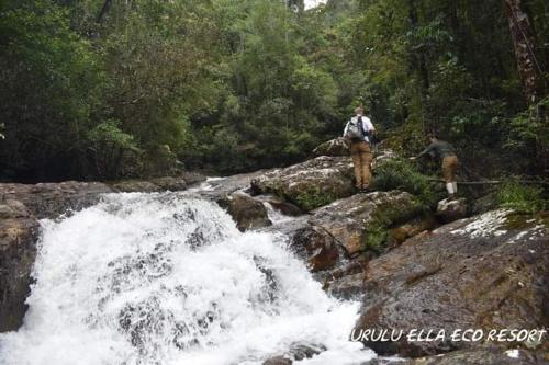 two people standing on rocks next to a waterfall at Sinharaja Kurulu Ella Eco Resort in Deniyaya