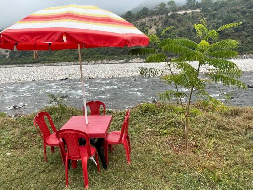 a red table with chairs and an umbrella next to a river at Nayar Valley Retreat in Lansdowne